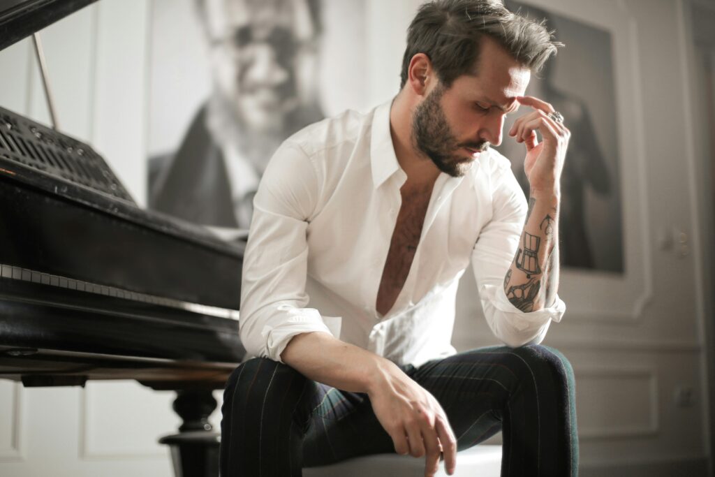 A pensive musician sits beside a piano in an elegant room, reflecting deeply.