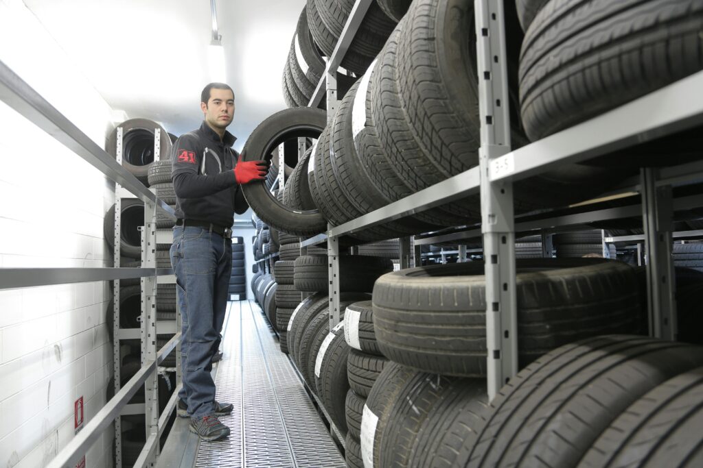 Mechanic places a tire on a rack in an indoor warehouse storage facility.