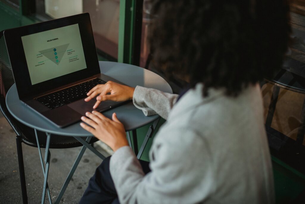 A woman working remotely on a laptop at an outdoor café table, focusing on a sales funnel diagram.